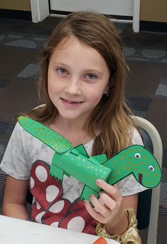 girl holding dinosaur craft she made